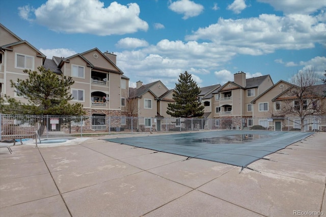 community pool with a community hot tub, a patio area, fence, and a residential view