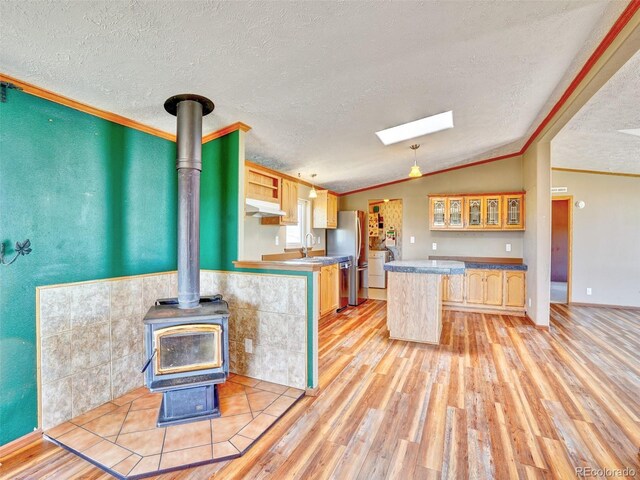kitchen with ornamental molding, lofted ceiling, light wood-type flooring, under cabinet range hood, and a sink