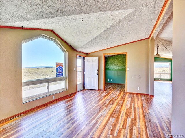 empty room featuring visible vents, a textured ceiling, wood finished floors, and vaulted ceiling