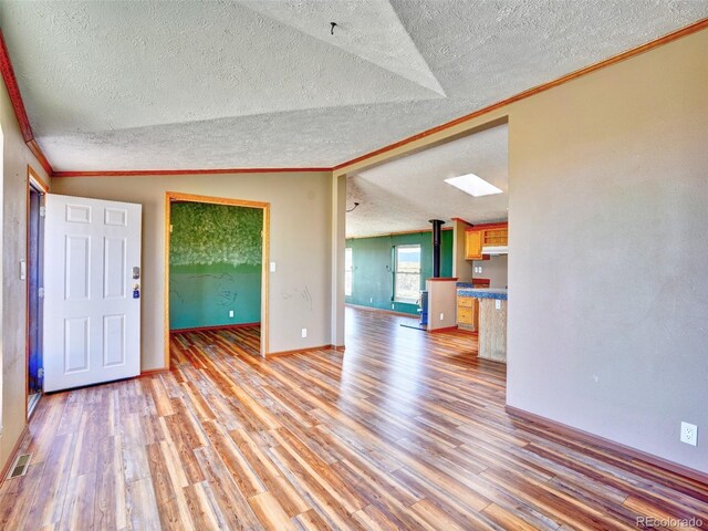 unfurnished living room featuring a textured ceiling, visible vents, crown molding, vaulted ceiling, and light wood finished floors