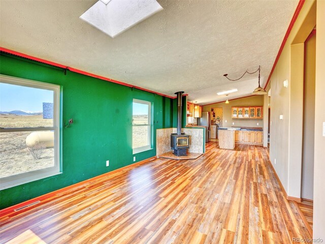 unfurnished living room featuring a textured ceiling, visible vents, a wood stove, lofted ceiling with skylight, and light wood-style flooring