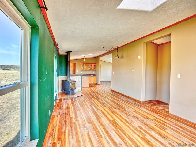 unfurnished living room with light wood-type flooring, a wood stove, a textured ceiling, and crown molding
