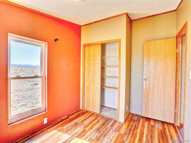 unfurnished bedroom featuring crown molding, a textured ceiling, a closet, and wood finished floors