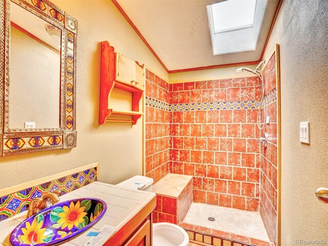 full bathroom with vaulted ceiling with skylight, a shower stall, vanity, toilet, and a textured wall