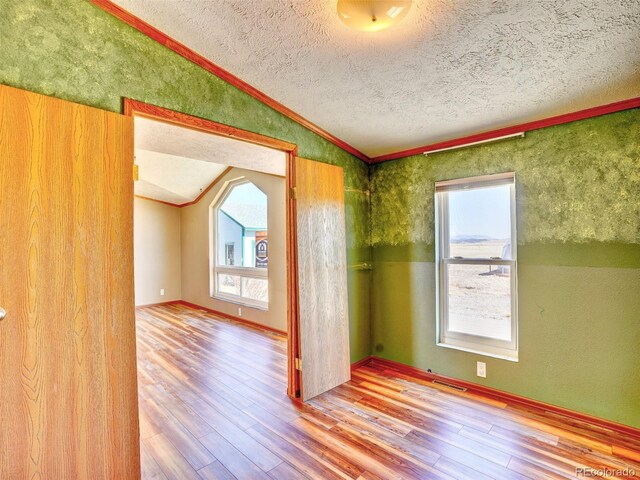 unfurnished room with a healthy amount of sunlight, visible vents, wood finished floors, and lofted ceiling