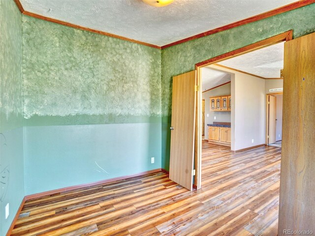 spare room with crown molding, a textured ceiling, baseboards, and wood finished floors