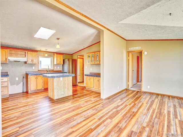 kitchen with vaulted ceiling with skylight, a textured ceiling, freestanding refrigerator, light wood finished floors, and under cabinet range hood