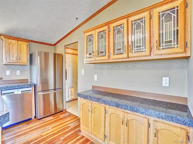 kitchen featuring tile counters, a textured ceiling, appliances with stainless steel finishes, and lofted ceiling