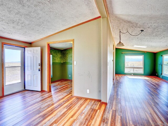 unfurnished room with a textured ceiling, ornamental molding, wood finished floors, and lofted ceiling