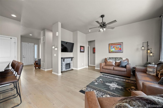 living area featuring light wood-style floors, ceiling fan, recessed lighting, a stone fireplace, and baseboards