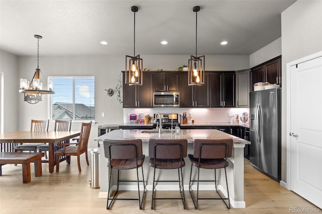 kitchen featuring stainless steel appliances, a sink, tasteful backsplash, an island with sink, and dark brown cabinetry