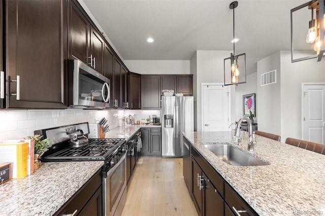 kitchen featuring stainless steel appliances, a sink, light wood-type flooring, dark brown cabinets, and light stone counters