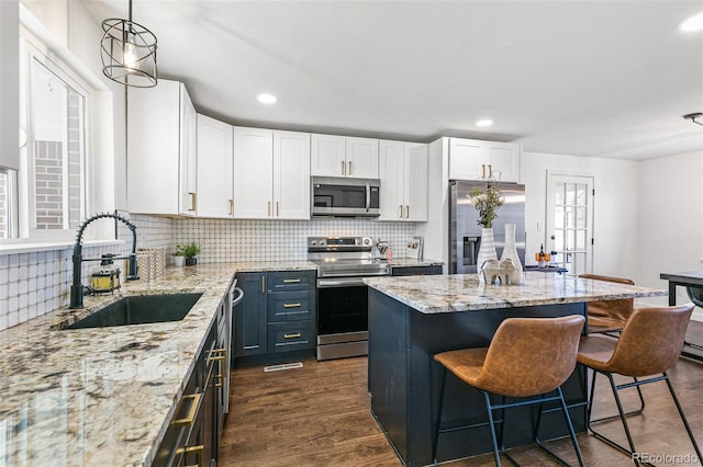 kitchen featuring stainless steel appliances, decorative light fixtures, white cabinets, light stone counters, and sink