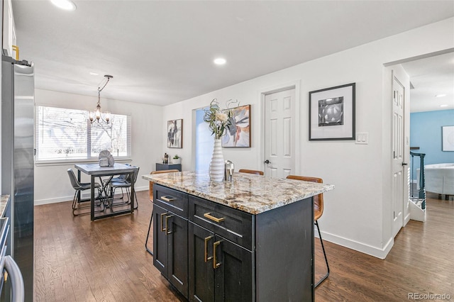 kitchen featuring dark hardwood / wood-style flooring, a kitchen island, pendant lighting, light stone counters, and a breakfast bar