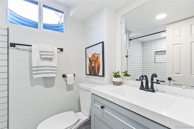 bathroom with toilet, a tile shower, and vanity