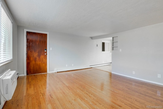 10491 W 7th Pl, Lakewood, CO 80215 - empty room featuring a baseboard radiator, a textured ceiling, wood finished floors, plenty of natural light, and a wall mounted air conditioner