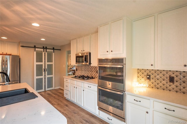 919 Taylor Ln, Erie, CO 80516 - kitchen featuring stainless steel appliances, a barn door, recessed lighting, light wood-style flooring, and white cabinets