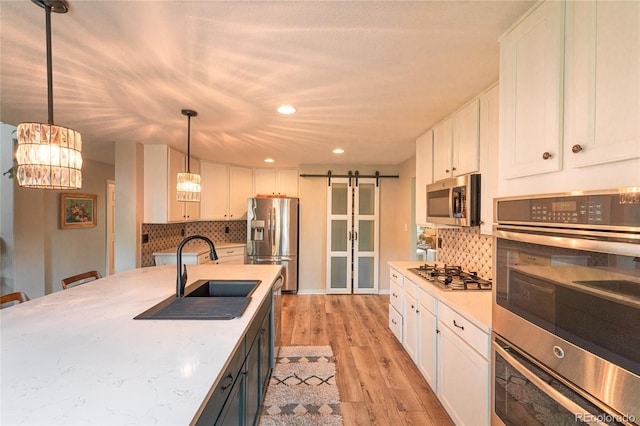 919 Taylor Ln, Erie, CO 80516 - kitchen featuring stainless steel appliances, a barn door, white cabinetry, light wood finished floors, and backsplash