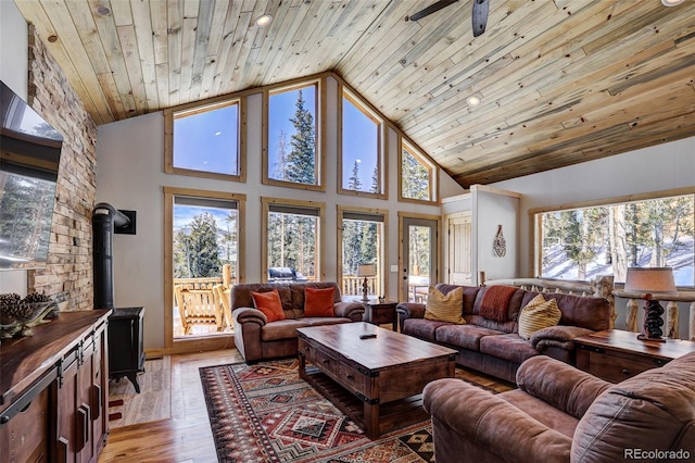 living room featuring high vaulted ceiling, light hardwood / wood-style floors, wooden ceiling, and a wood stove