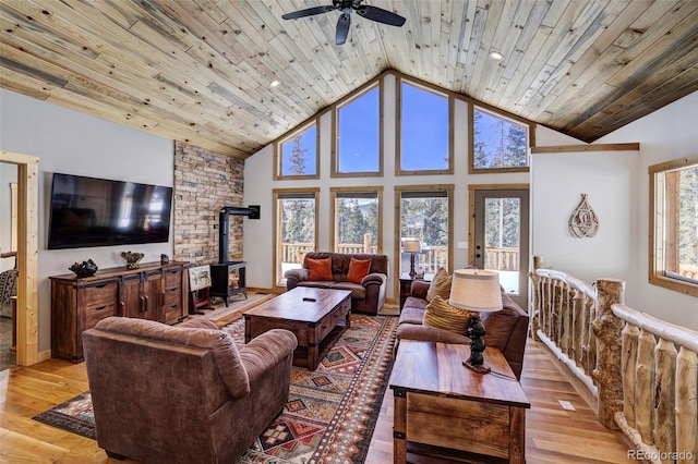 living room with high vaulted ceiling, a ceiling fan, light wood-style floors, wood ceiling, and a wood stove