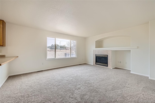 unfurnished living room with a tile fireplace, light colored carpet, and a textured ceiling