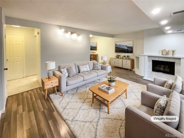 living room featuring a tiled fireplace, hardwood / wood-style floors, and a textured ceiling