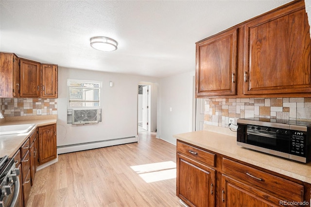 kitchen featuring decorative backsplash, light wood-type flooring, stainless steel appliances, baseboard heating, and sink