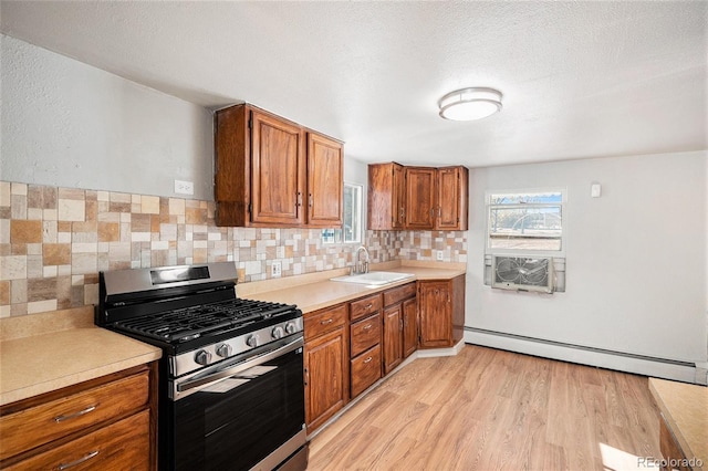 kitchen with sink, baseboard heating, backsplash, stainless steel range with gas stovetop, and light wood-type flooring