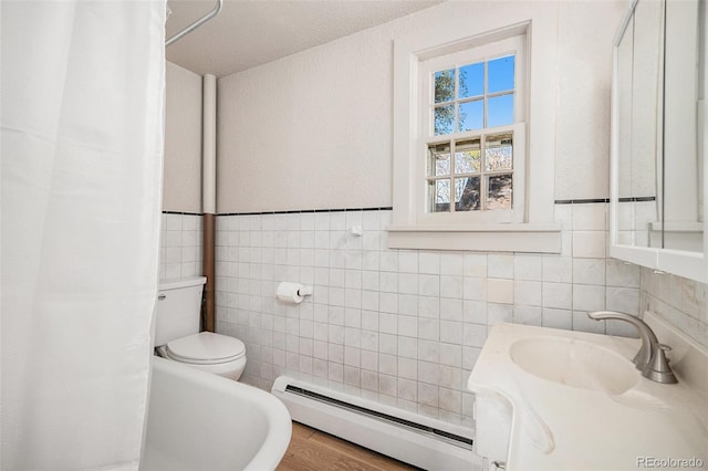 bathroom featuring wood-type flooring, toilet, tile walls, and a baseboard heating unit