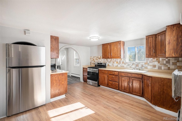 kitchen with light wood-type flooring, backsplash, stainless steel appliances, baseboard heating, and sink