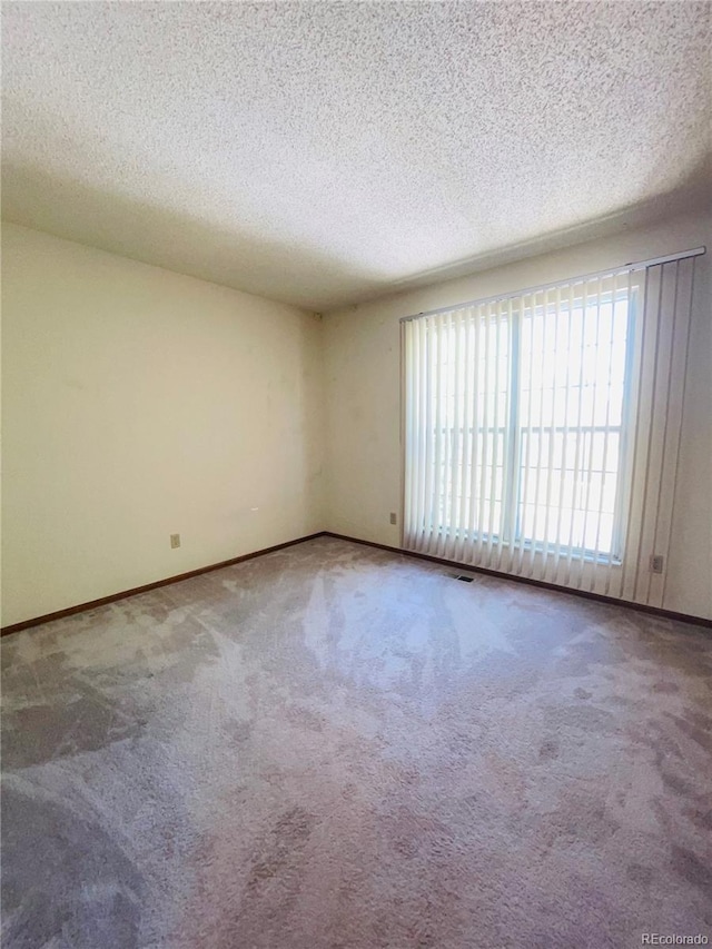 spare room featuring carpet flooring, baseboards, and a textured ceiling