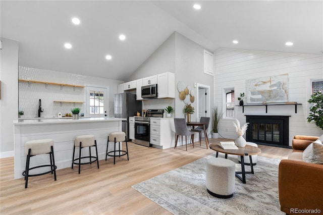 living room featuring high vaulted ceiling, a brick fireplace, and light hardwood / wood-style floors