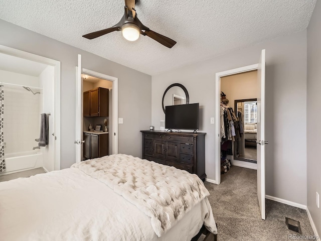 carpeted bedroom featuring a walk in closet, a textured ceiling, ceiling fan, connected bathroom, and a closet