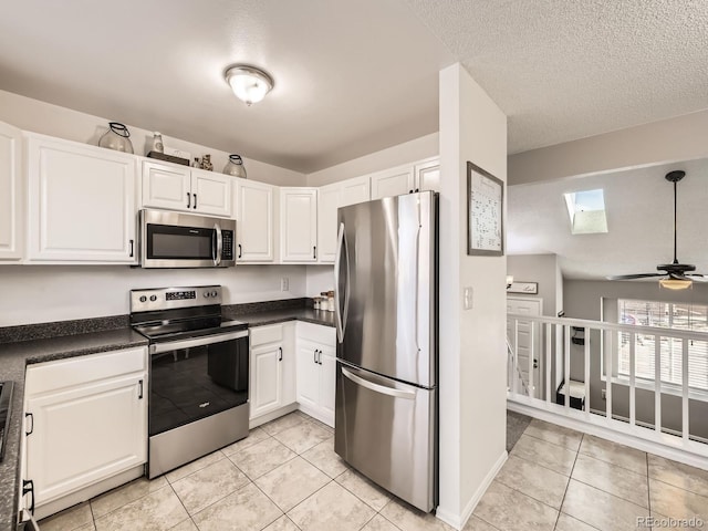 kitchen featuring a skylight, white cabinetry, ceiling fan, light tile patterned floors, and appliances with stainless steel finishes