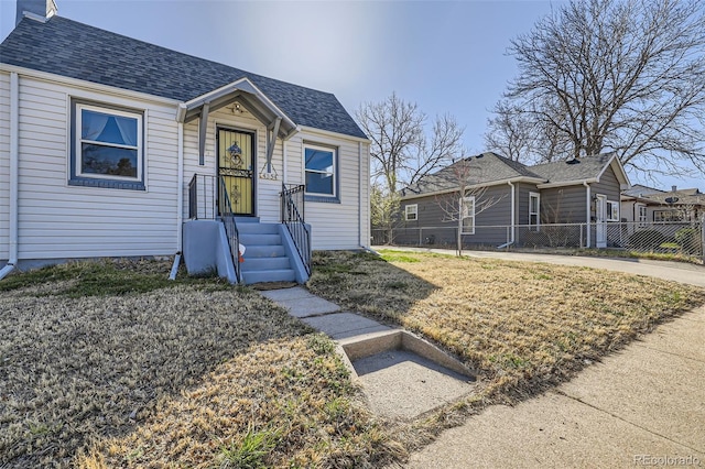 bungalow-style house with fence, roof with shingles, and a front yard