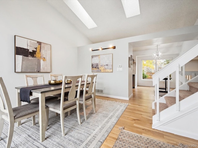 dining area featuring a notable chandelier, stairway, visible vents, lofted ceiling with skylight, and wood finished floors