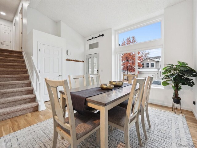 dining room featuring high vaulted ceiling, stairway, light wood-style flooring, and baseboards
