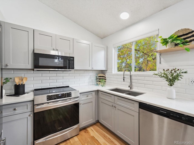 kitchen with light countertops, a sink, lofted ceiling, stainless steel appliances, and gray cabinetry