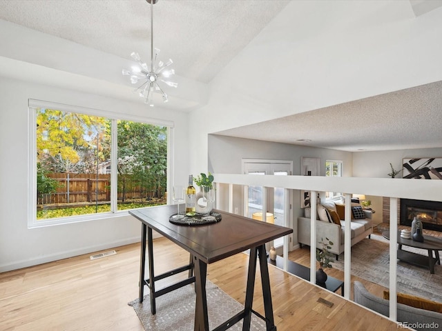 dining room with visible vents, an inviting chandelier, light wood-type flooring, a textured ceiling, and a glass covered fireplace