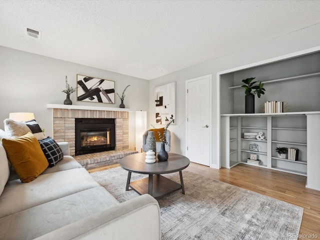 living room featuring a textured ceiling, wood finished floors, a brick fireplace, and visible vents