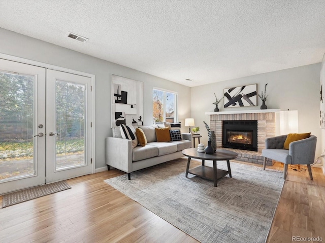 living area featuring french doors, a textured ceiling, light wood-style floors, visible vents, and a brick fireplace