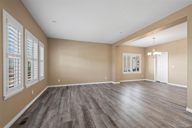 unfurnished room with visible vents, plenty of natural light, an inviting chandelier, and wood finished floors