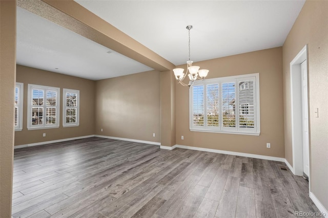 spare room featuring baseboards, a notable chandelier, and wood finished floors