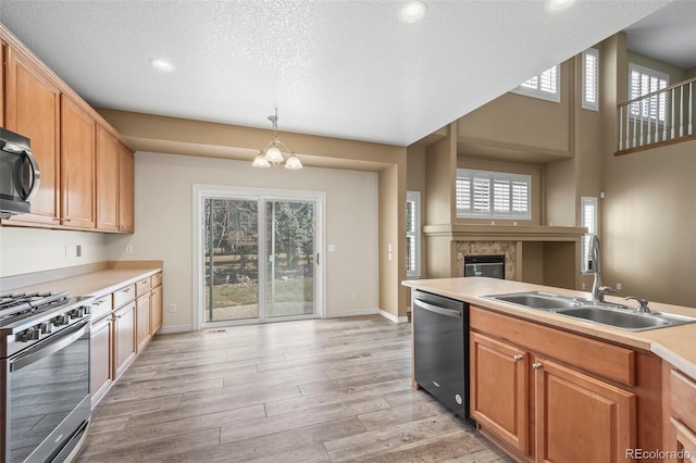 kitchen featuring light wood-type flooring, light countertops, a glass covered fireplace, stainless steel appliances, and a sink