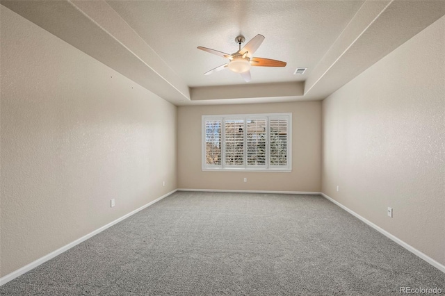 carpeted empty room featuring visible vents, ceiling fan, baseboards, and a tray ceiling