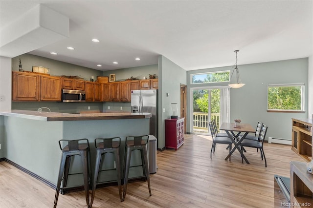 107 Mountain Vista Ln, Silverthorne, CO 80498 - kitchen featuring appliances with stainless steel finishes, brown cabinets, a kitchen breakfast bar, a baseboard heating unit, and light wood-type flooring