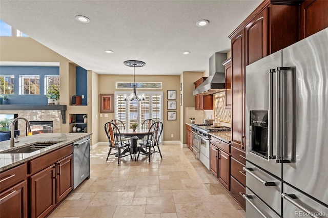 kitchen featuring sink, hanging light fixtures, high end appliances, light stone counters, and wall chimney exhaust hood