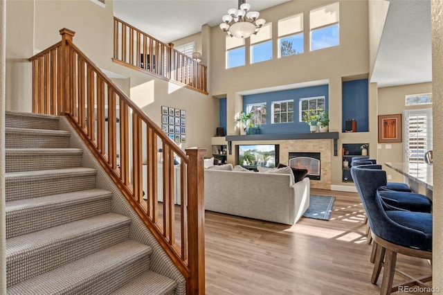 living room with a notable chandelier, a towering ceiling, a fireplace, and light hardwood / wood-style floors