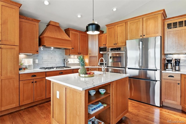 6776 Salvia Ct, Arvada, CO 80007 - kitchen featuring stainless steel appliances, custom range hood, light wood finished floors, tasteful backsplash, and a center island with sink