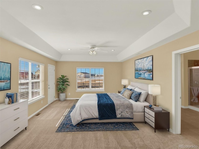 bedroom with ceiling fan, light colored carpet, multiple windows, and a tray ceiling